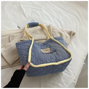 Close-up of blue quilted canvas tote bag featuring cute mini bear embroidery and yellow straps