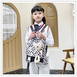 Détail d'un sac à dos enfant à damier noir et blanc avec un ours en peluche sur une fillette