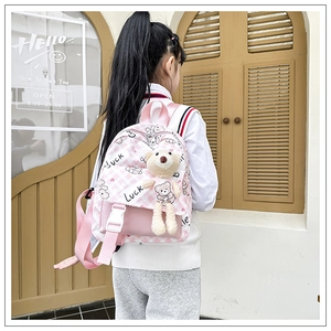 Détail du sac à dos enfant à carreaux roses avec charm ours en peluche porté par un enfant