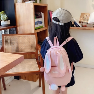 Pink cartoon rabbit backpack for girls with long ears and plush ball in a cozy room