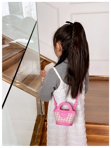 Pink plaid bucket bag with top handle and shoulder strap shown in a modern interior setting