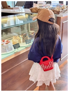 Detail of red gingham mini bucket bag with leather trim worn by a child in a cafe