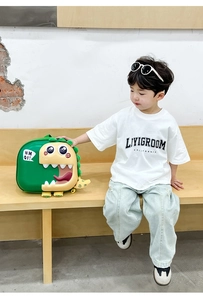 Detail shot of the 3D green dinosaur backpack with spikes worn by a boy on a wooden bench