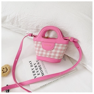 Detail of pink plaid mini handbag with gold brand logo and adjustable strap on a book