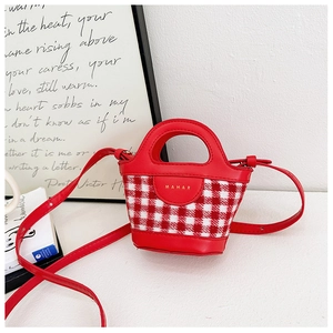 Detailed view of mini red gingham handbag with leather handles on a white tabletop