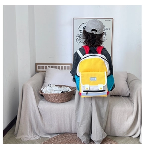 Rear view of child wearing colorful yellow backpack with blue straps and white front pocket