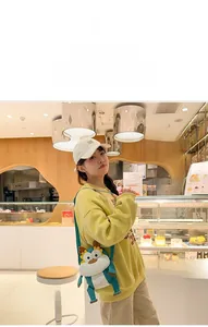 Sac bandoulière peluche dragon porté par un mannequin dans un café chaleureux
