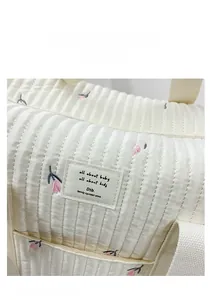 Detailed close-up of quilted ivory fabric with pink floral embroidery on a stylish diaper bag