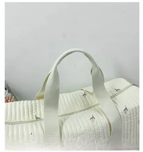Detail of quilted white travel bag featuring delicate pink floral embroidery and handle