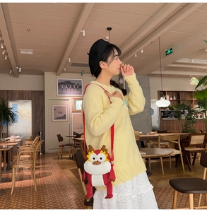 Vue détaillée du sac bandoulière dragon rouge en peluche sur un mannequin dans un café