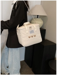 Close-up of beige canvas diaper bag with cute bear embroidery and adjustable shoulder strap