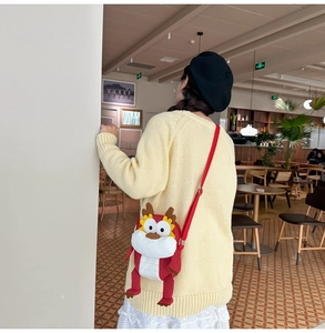 Détail d'un sac bandoulière dragon rouge en peluche porté dans un décor de café