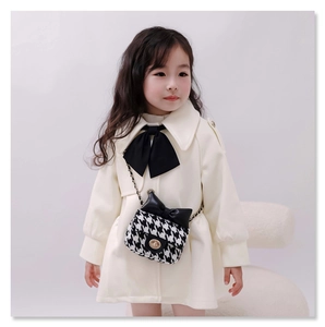 Detail of girls tweed crossbody bag with black bow and gold chain strap on white coat
