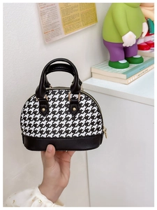 Detail of mini houndstooth shell handbag with golden hardware and black PU leather trim