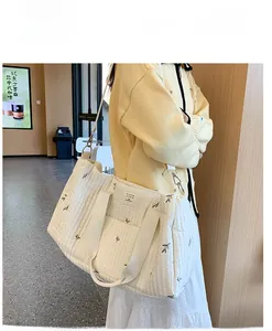 Quilted beige diaper bag with leaf embroidery and detachable strap worn by model