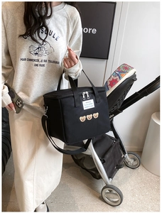 Detail of black diaper bag with bear embroidery attached to a stroller in street setting