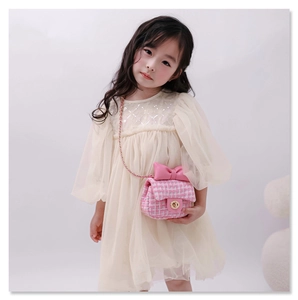 Pink tweed kids' crossbody bag with bow detail shown on child model in soft studio lighting