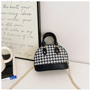 Close-up of mini shell-shaped handbag with black and white houndstooth pattern and gold chain