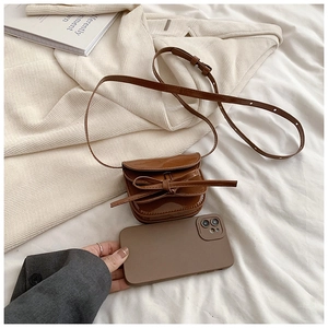Detail view of mini brown patent leather bag with bow decoration and adjustable strap