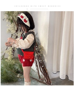 Close-up of a red mini tassel bag styled with a vintage baby girl outfit and green vest