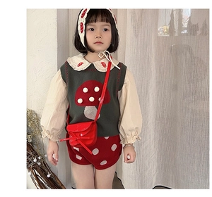 Detail of child green knit vest with 3D mushroom accent and red patent leather crossbody bag