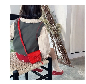 Rear side view of a red patent leather mini crossbody bag with bow on a child model