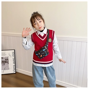 Kind trägt schwarze Dino-Umhängetasche mit roter Strickweste und blauen Jeanshosen