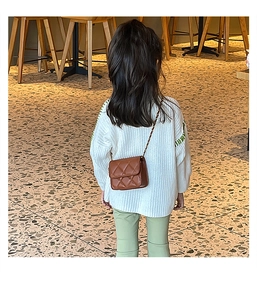 Girl wearing a brown quilted mini crossbody bag with a metal chain in a warm room