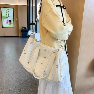 Quilted white canvas diaper bag with floral embroidery and adjustable shoulder strap