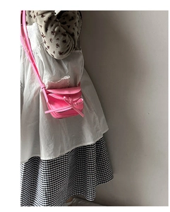 Detail of a bright pink mini crossbody bag featuring a cute bow and thin strap on a model