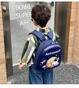 Rear view of child wearing blue hard shell astronaut backpack on outdoor city street