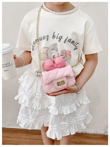 Girl's pink quilted crossbody bag with large bow and gold chain strap in life scene