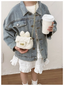 Close-up of white quilted crossbody bag with bow decoration and golden chain strap