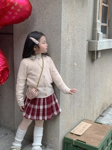 Toddler girl wearing beige knit cardigan, red plaid skirt, and pink round chain mini bag