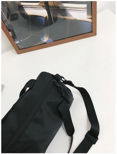 Detail view of the black cylindrical canvas bag with adjustable strap and top zipper