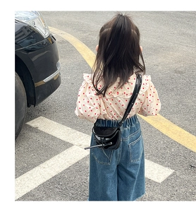 Rear view of a black patent leather mini saddle bag with thin strap on a stylish child