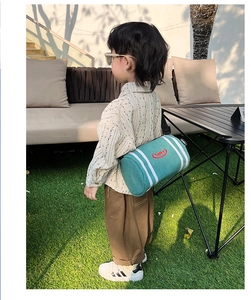 Outdoor lifestyle view of a green kids' canvas crossbody bucket bag with white stripes