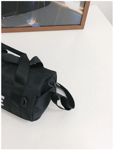 Top view of a black cylindrical canvas crossbody bag with white letter print and straps