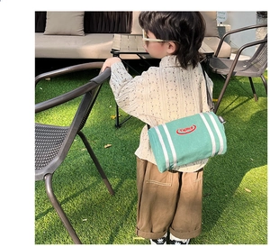 Close-up of children's green canvas bucket bag with vertical stripes on an outdoor lawn