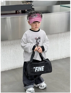 Kids black cylinder canvas crossbody bag with white FINE print shown in a street style view