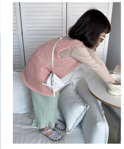Girl wearing pink knitted vest with green pleated skirt and a white knotted crossbody bag