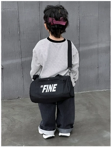Close-up of black cylinder crossbody bag with FINE print and adjustable strap for kids