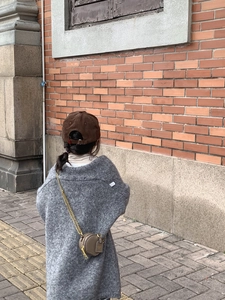 Outdoor view of children's round leather mini crossbody bag with gold chain and gray cardigan
