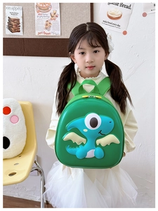 Front view of green hard shell backpack with 3D cartoon dinosaur worn by young girl