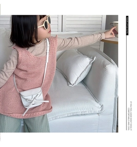 Detailed close-up of a pink knit vest and white bow crossbody bag on a child outfit