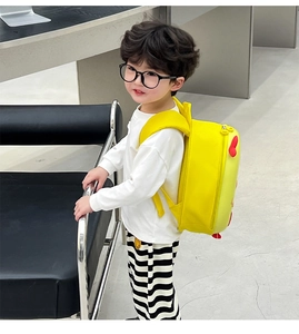 Side view of a bright yellow kid's eggshell backpack with red heart detail on a boy