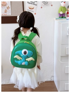 Detail view of the green dinosaur shell backpack worn by a child in a home setting