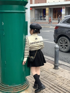 Detail of a black mini round bag with a bronze chain strap on a striped sweater