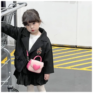 Detailed view of pink heart-shaped mini crossbody bag on child model in street setting