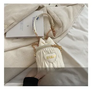 Détail d'un sac seau blanc matelassé avec nœud décoratif et garniture cœur doré